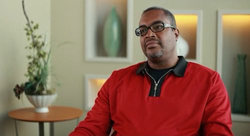 Calvin Mays Jr. is shown from the waist up, sitting in a chair in a waiting room
